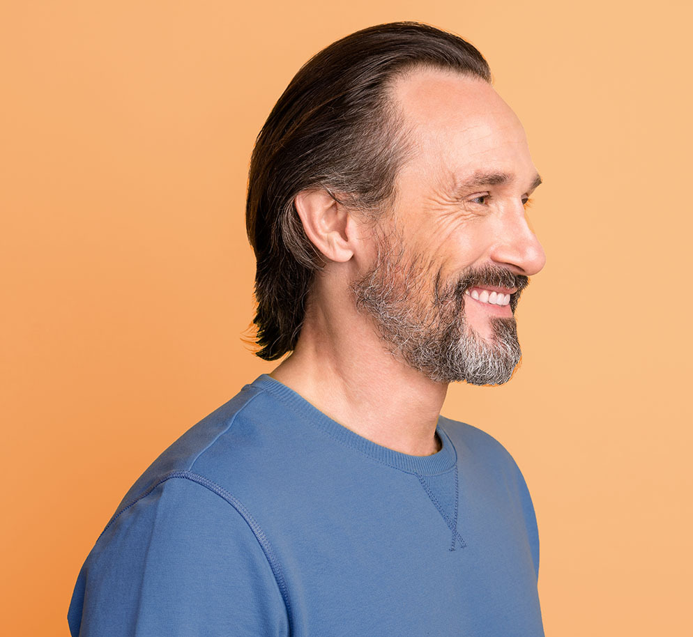 Side profile of a smiling man standing against an orange background