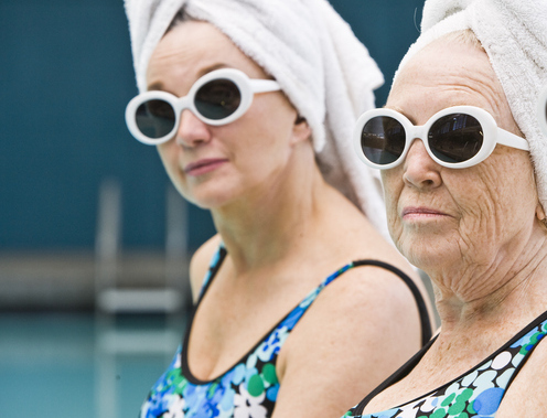 Two women wearing sunglasses and towels at the pool